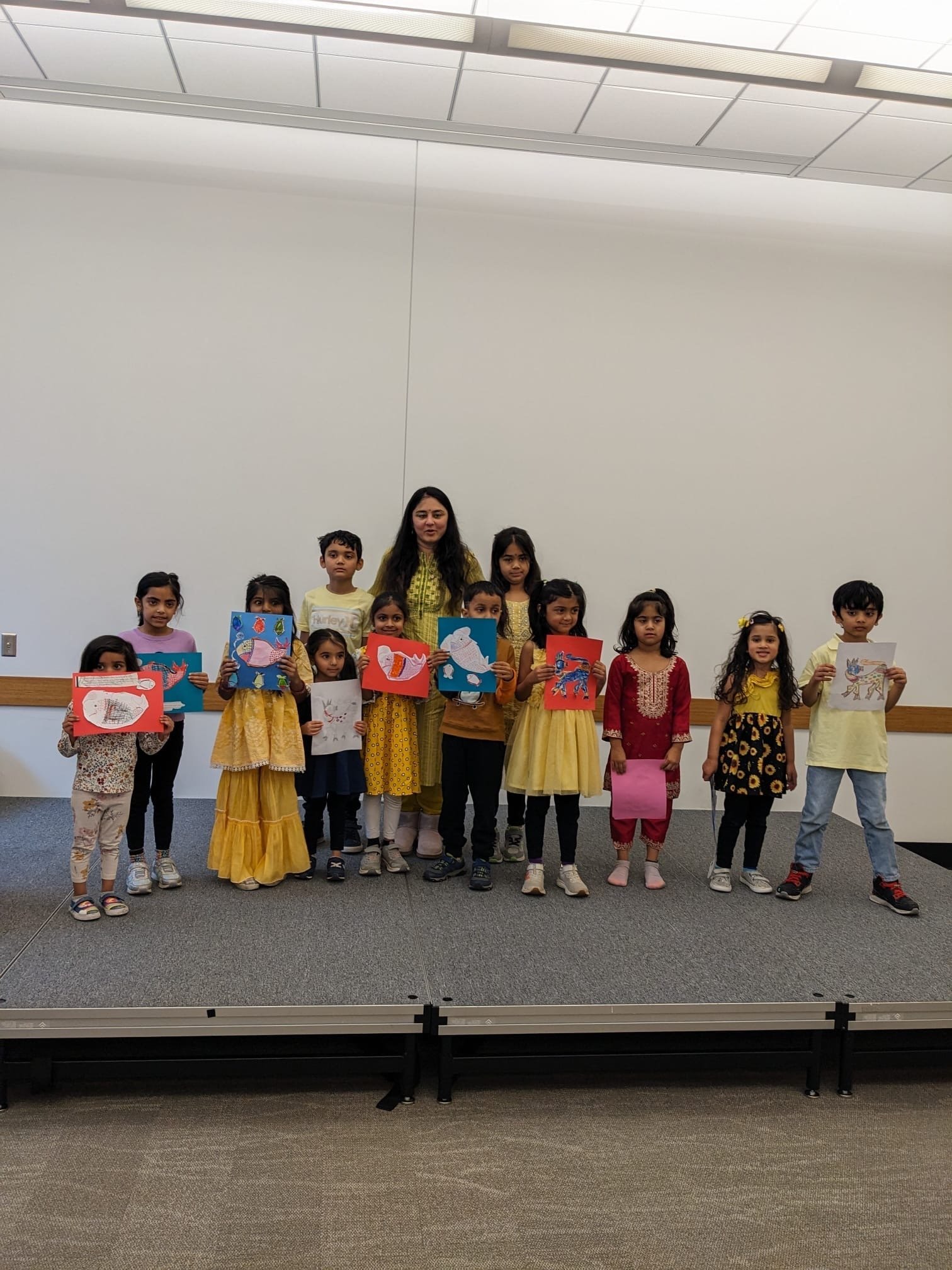 Children on stage proudly holding their Madhubani and folk-art inspired artwork