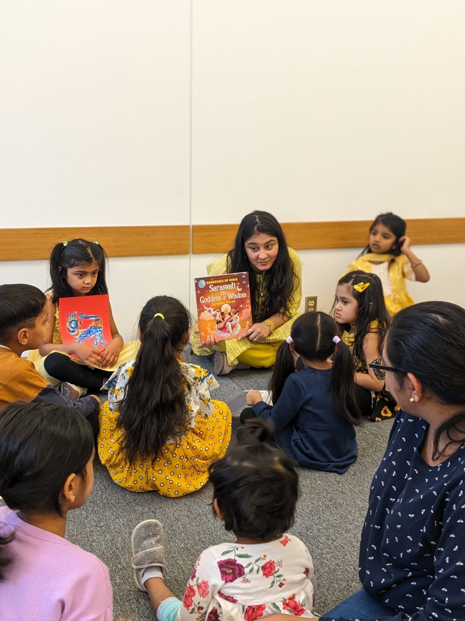 Divvya A. Singh holding a copy of Saraswati: Goddess of Wisdom while reading to a circle of children