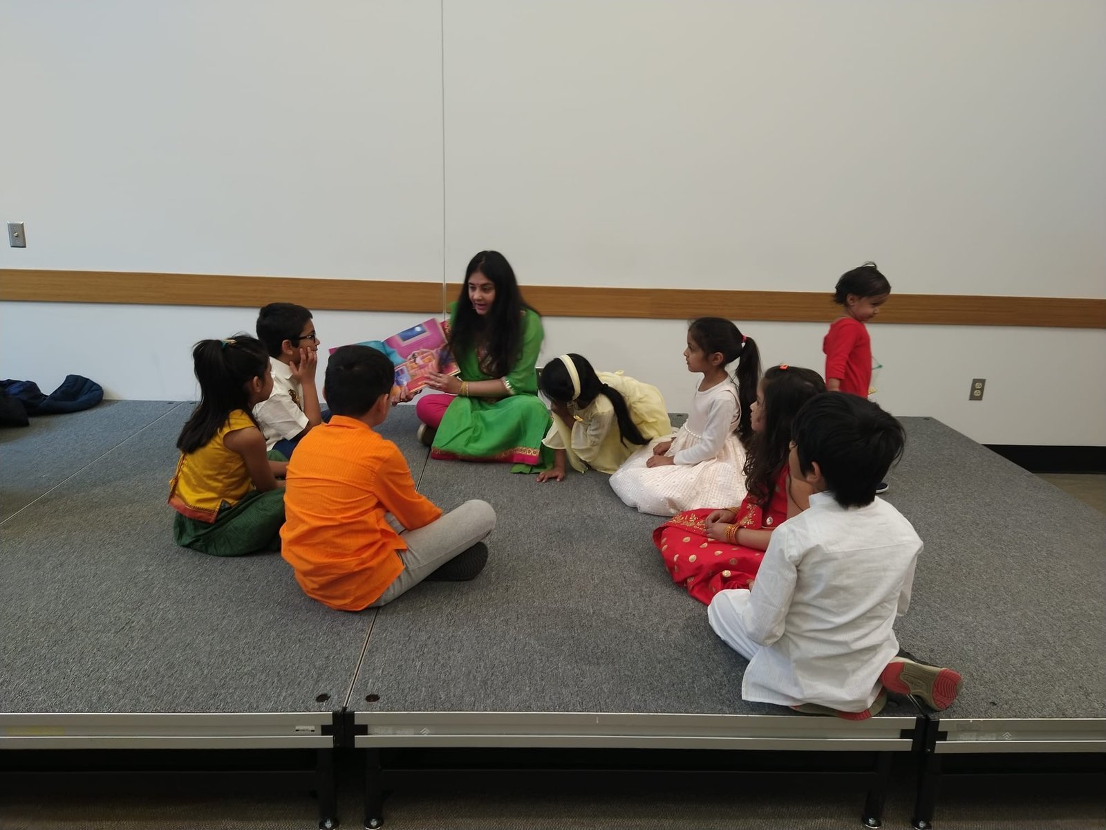 Children and Divvya seated on a stage floor for a storytelling session